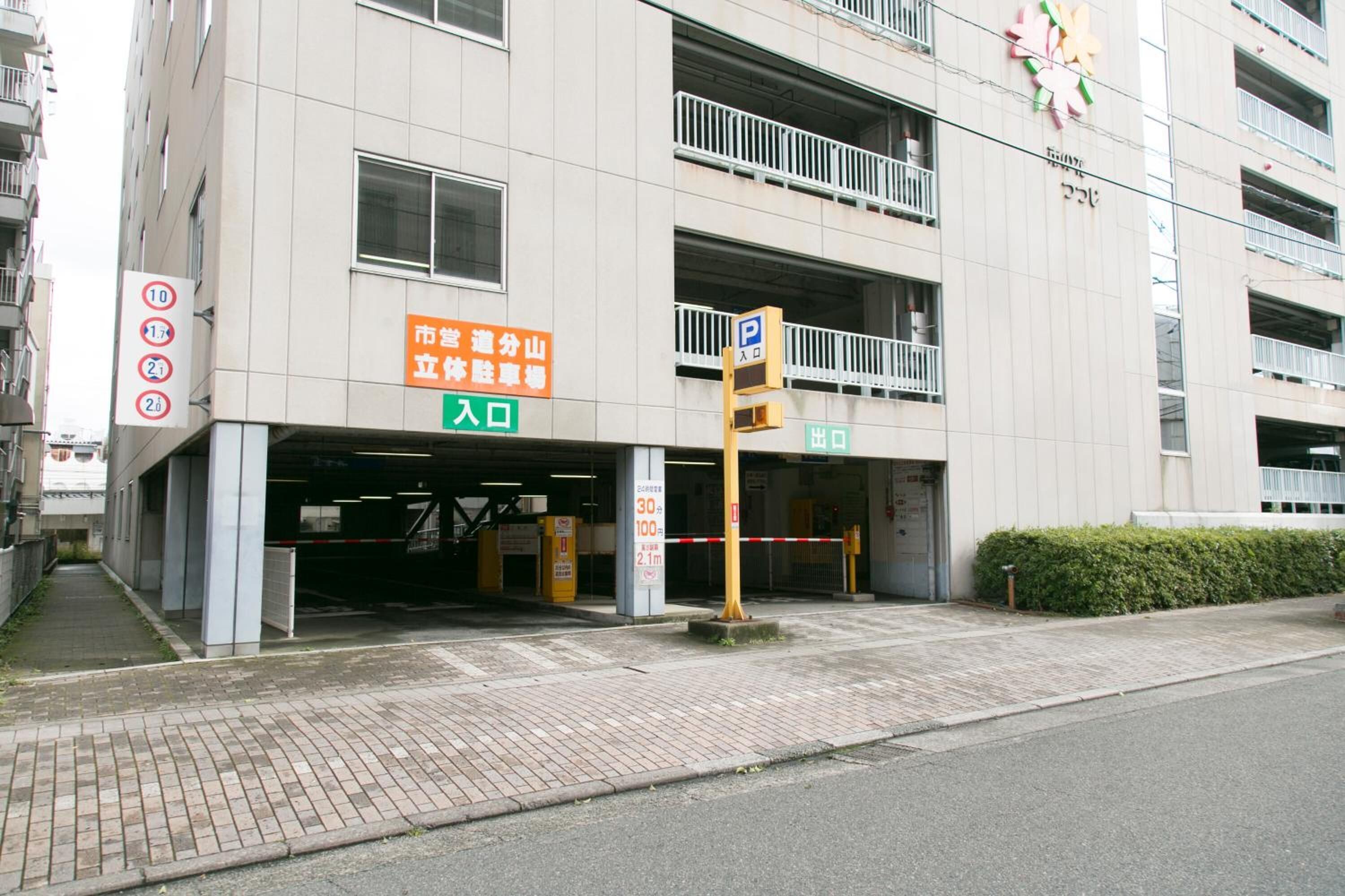 Un edificio de varios pisos con entrada a un estacionamiento, un sendero para peatones y un letrero que indica un límite de estacionamiento de 30 minutos.