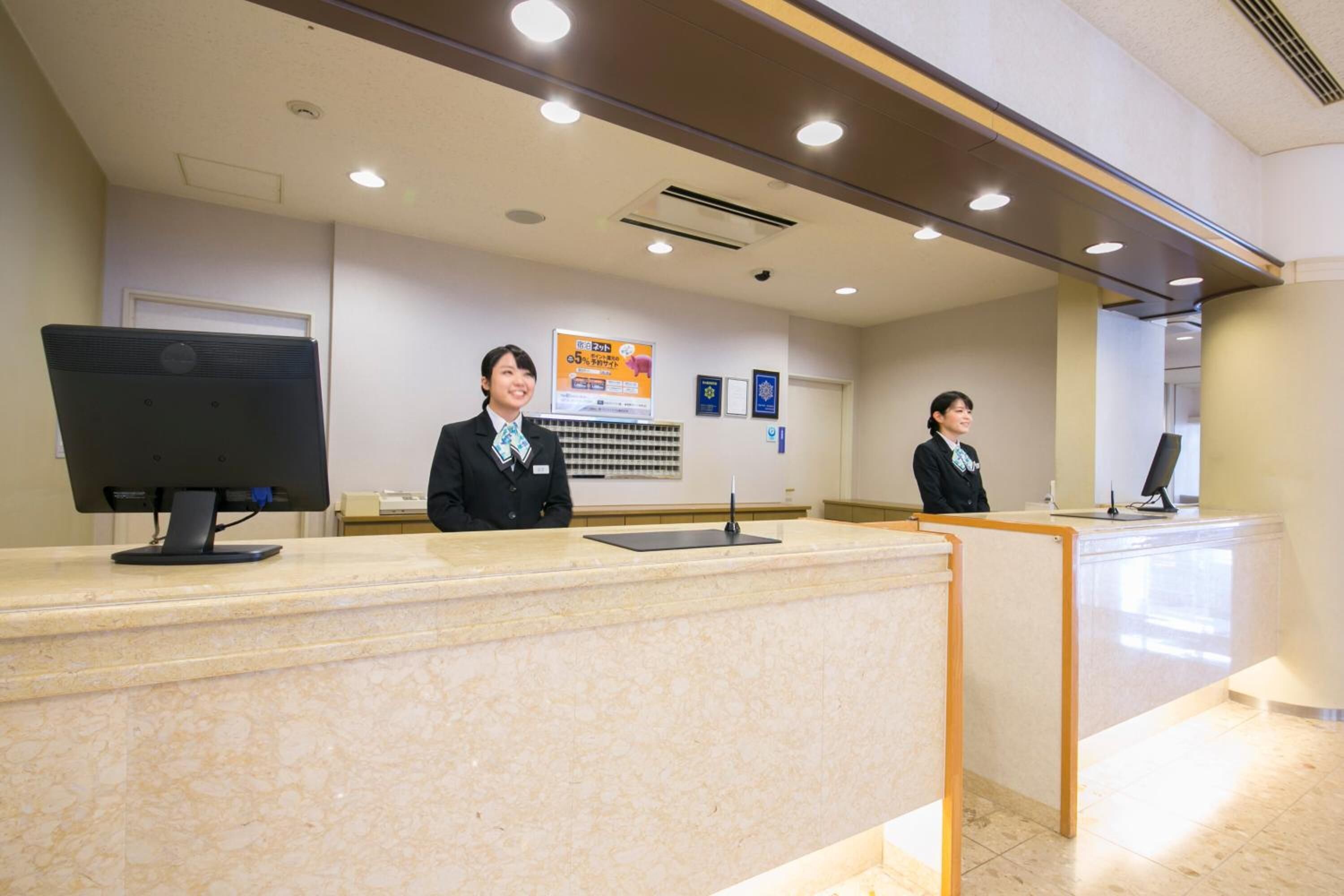 A reception area with a marble counter, two receptionists, a computer monitor, and a framed award on the wall.