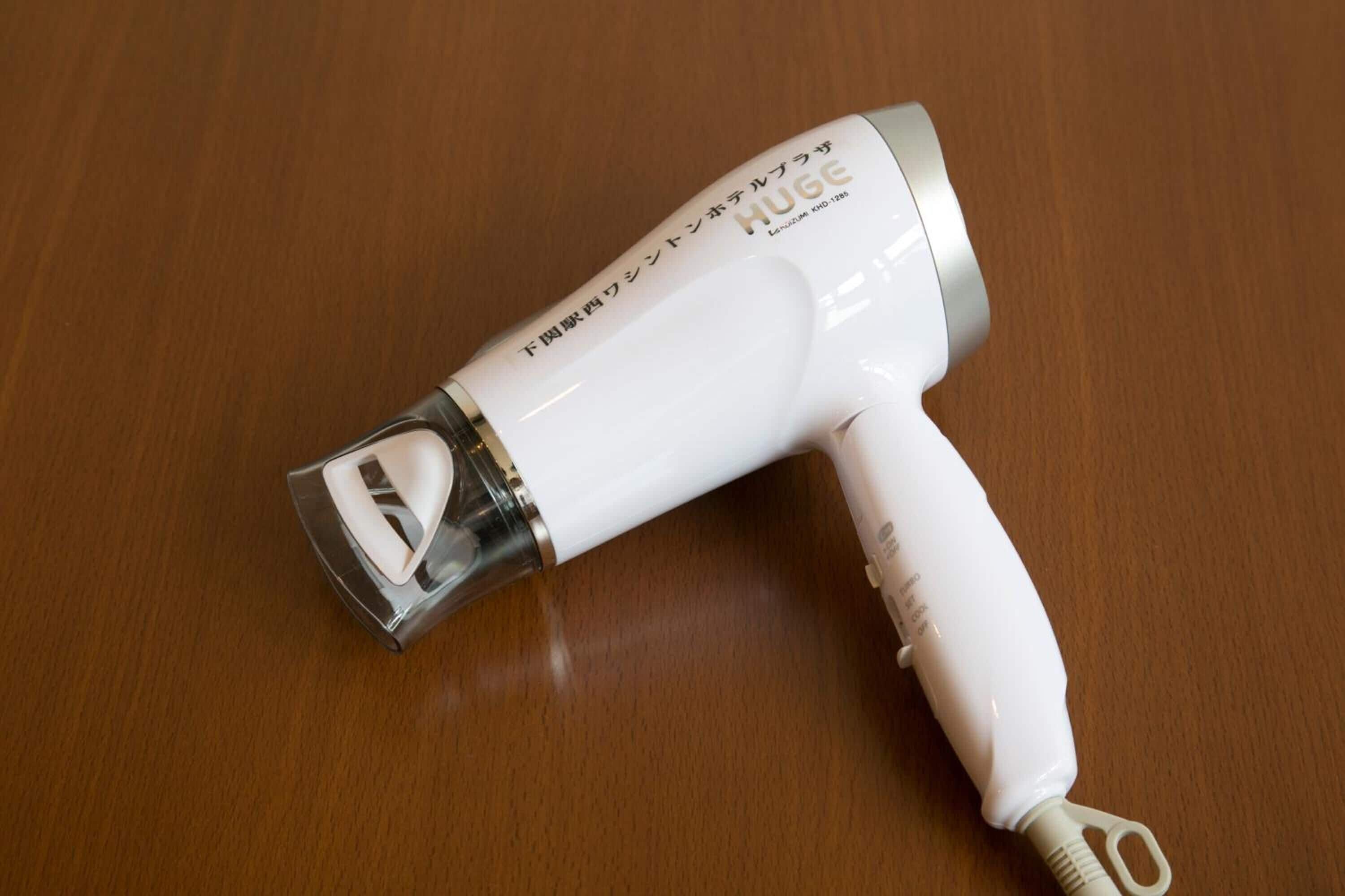 Un secador de pelo blanco con una sección transparente y texto en japonés sobre una superficie de madera.