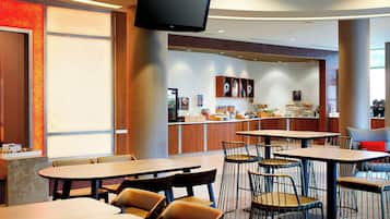 Un restaurant avec plusieurs tables et chaises, un comptoir où sont exposés des plats, et un téléviseur fixé au mur.