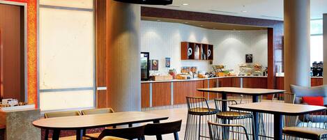 A restaurant with multiple tables and chairs, a counter with food items, and a television mounted on the wall.