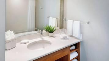 A modern bathroom with a white sink, a mirror, a potted plant, and a wooden vanity.