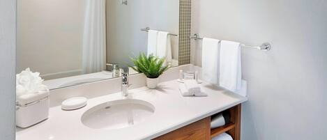 Un baño moderno con un lavamanos blanco, un espejo, una planta en maceta y un mueble de tocador de madera.