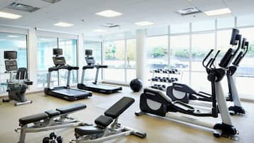 A well-lit gym with various exercise equipment, large windows, and a view of the outside.