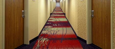 Un pasillo de hotel con pisos alfombrados, puertas de madera y lámparas fijadas a la pared.