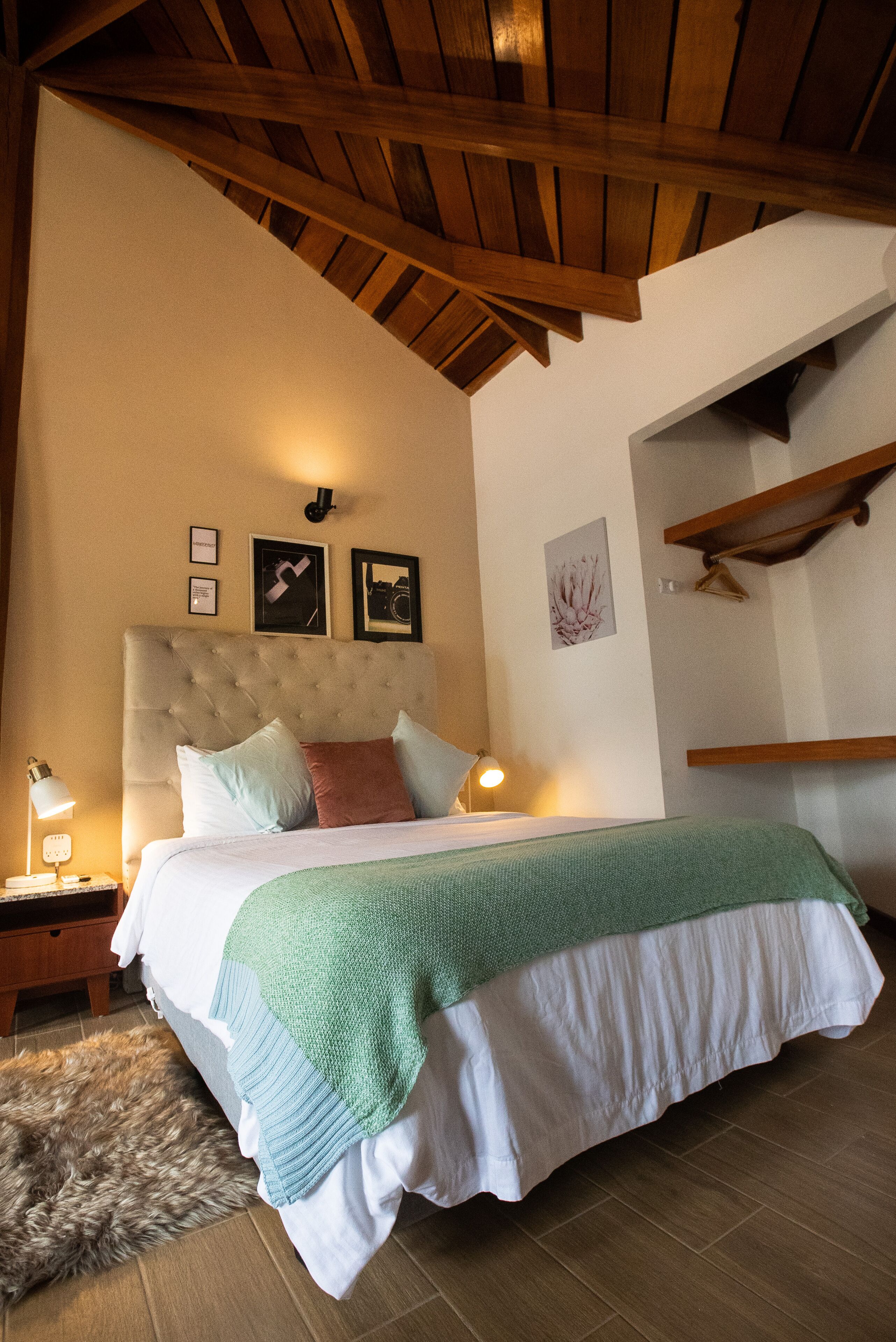 A bedroom with a tufted headboard, a bed with a green and white bedspread, a wooden nightstand with a lamp, and a fluffy rug.