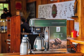A coffee machine with a box labeled 'EXPERIENCIA GOURMET' and two thermos cups beside it. - Camino Verde Bed & Breakfast (Monteverde)