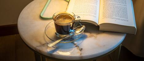 A round table with a book, a cup of coffee, and a spoon. A blue lamp is on the table, and a green pen is on the book.