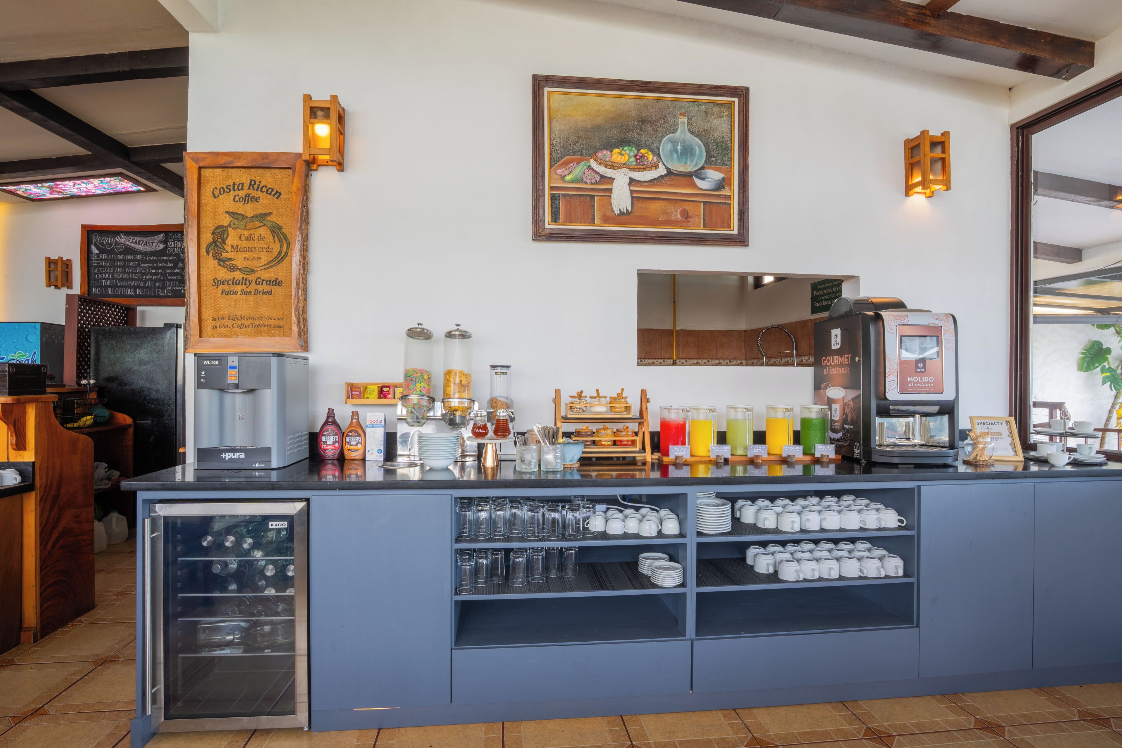 A coffee shop counter with a coffee machine, beverage dispensers, and a variety of cups and mugs.