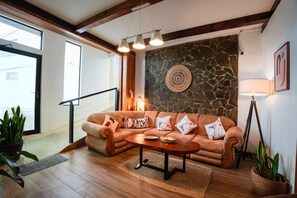 A modern living room with a stone accent wall, a brown leather sofa, a wooden coffee table, and a staircase leading to an upper floor.