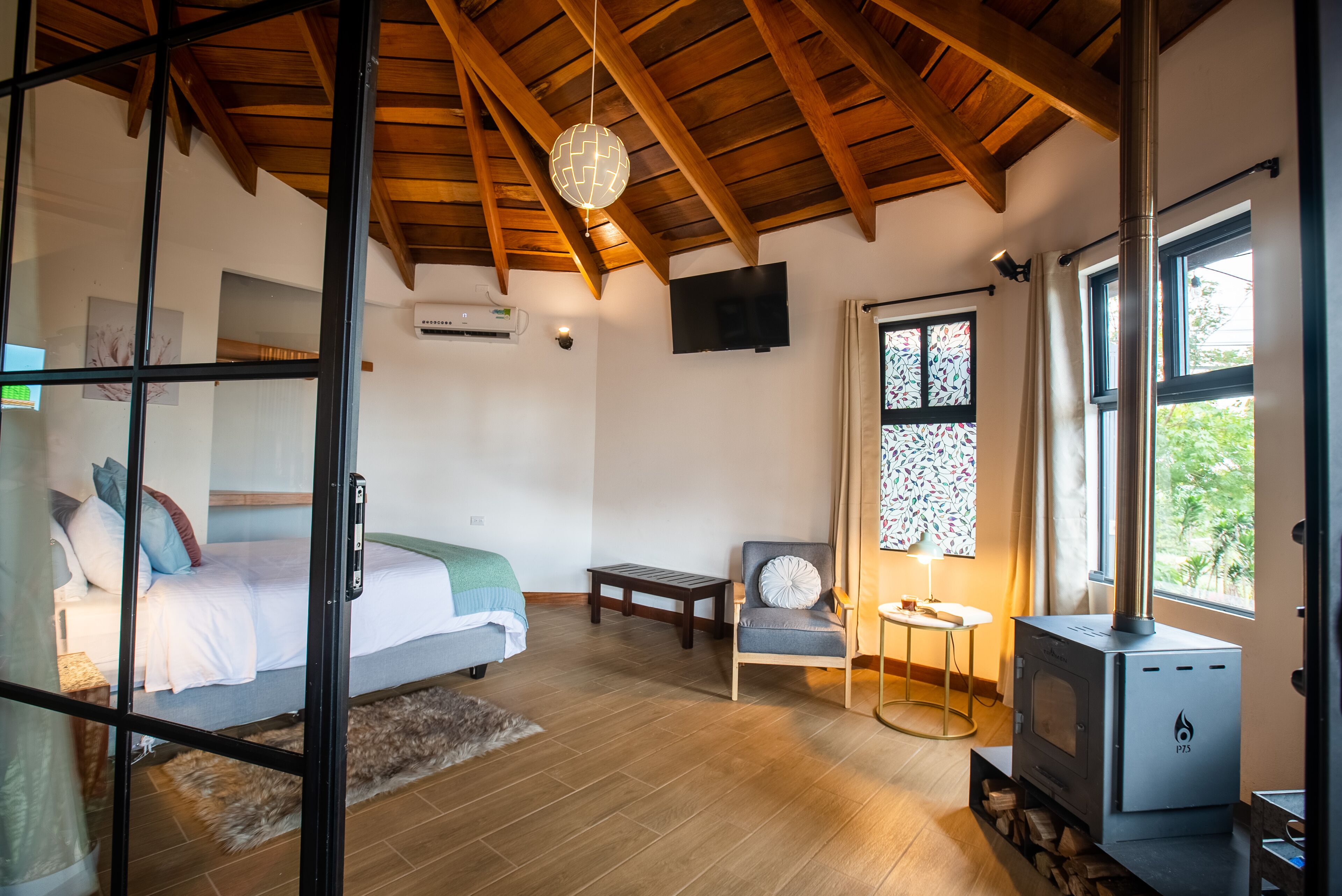 Una habitación acogedora con cama, una silla, una mesita, televisor y estufa de leña.