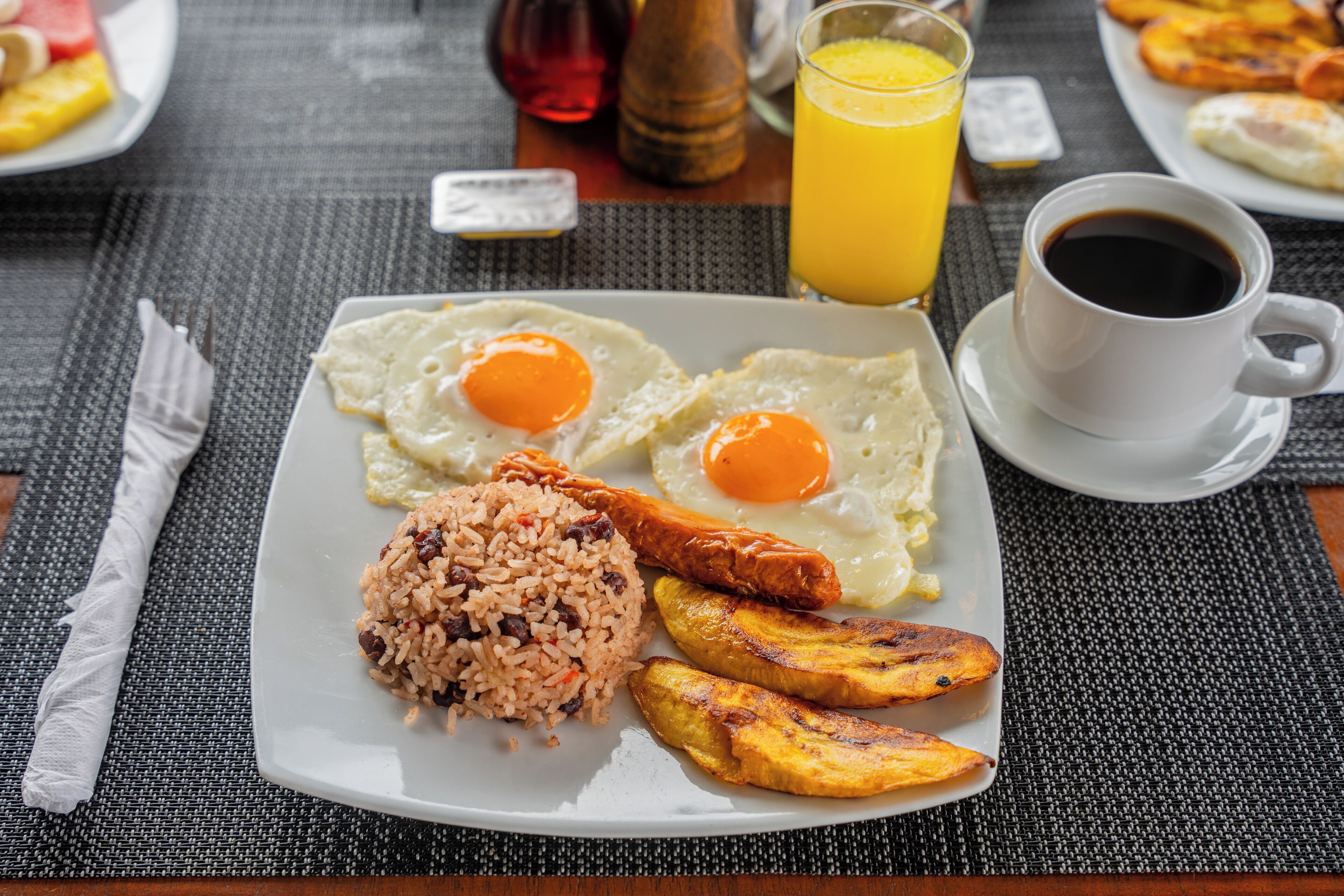 Un plato de desayuno con huevos, arroz, plátanos maduros y una taza de café.