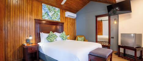Habitación de hotel con techo de madera, cama con ropa de cama blanca, televisor sobre un mueble bajo y unidad de aire acondicionado.