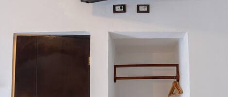 A room with a dark wooden door, a mounted flat-screen TV, a wooden shelf, and a hanging clothes rack.