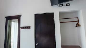 A room with a ceiling fan, a flat-screen TV mounted on the wall, a wooden bench, a door, and a small wooden shelf.