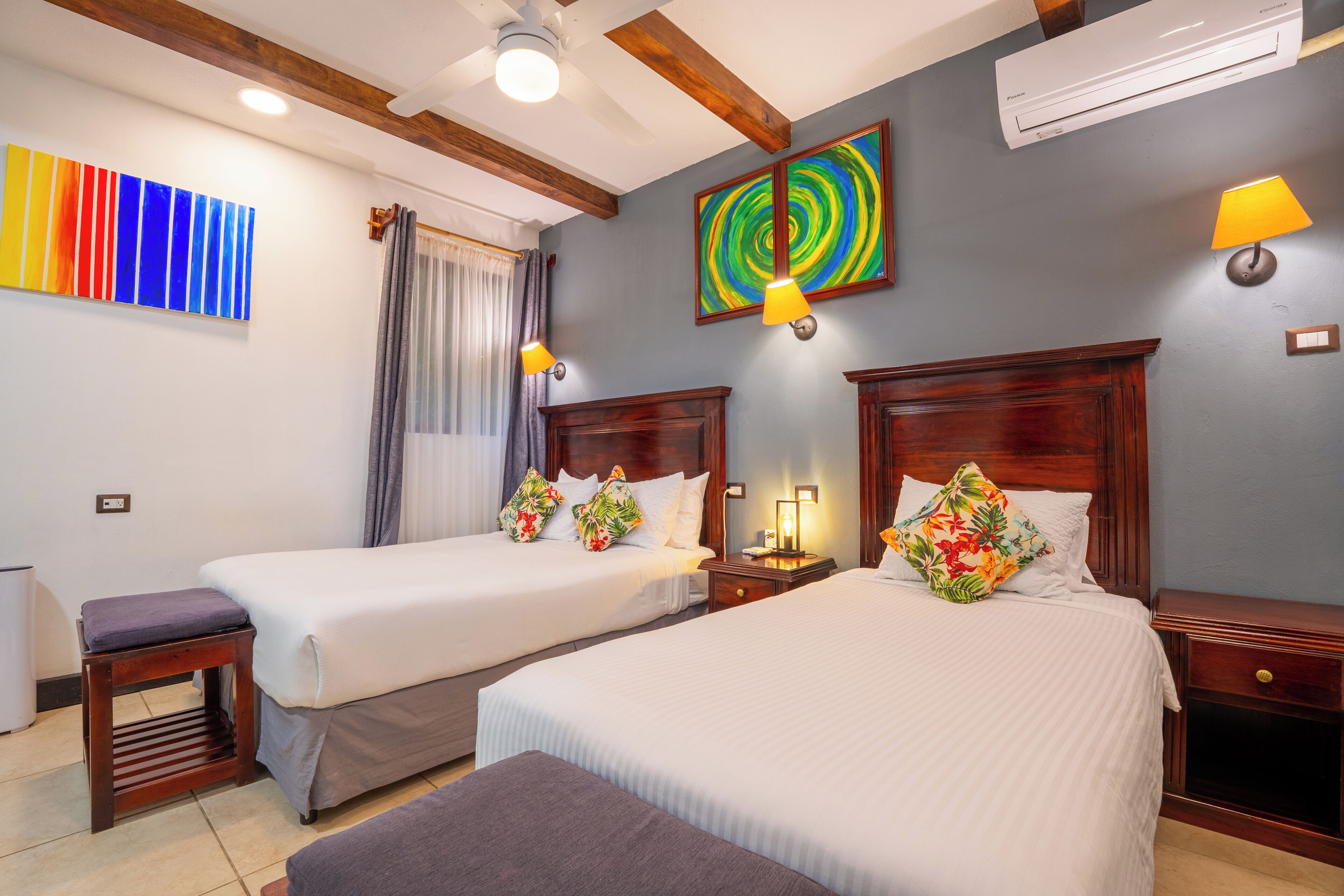 A hotel room with two beds, a wooden headboard, a nightstand, a lamp, and a ceiling fan.