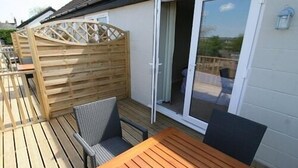 Eine Holzterrasse mit Tisch und Stühlen, einer Schiebetür und einem Holzzaun.