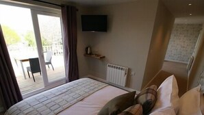 Ein Schlafzimmer mit einem Bett, Kissen, einem an der Wand befestigten Fernseher und Blick ins Freie durch eine Schiebetür.