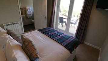 A bedroom with a bed, a radiator, a bathroom door, and a view of the outside.