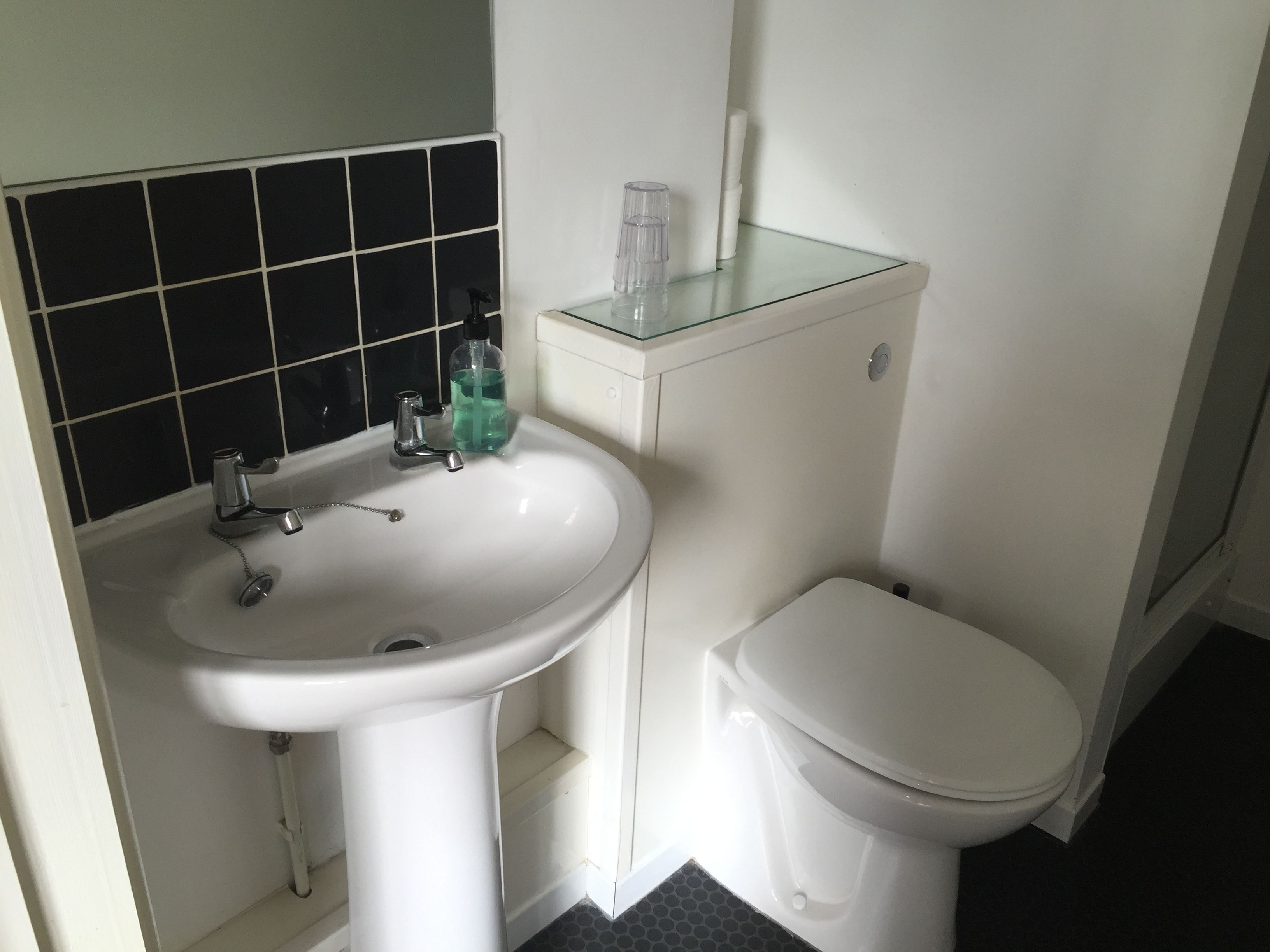 A bathroom with a white sink, black tiled backsplash, and a white toilet.