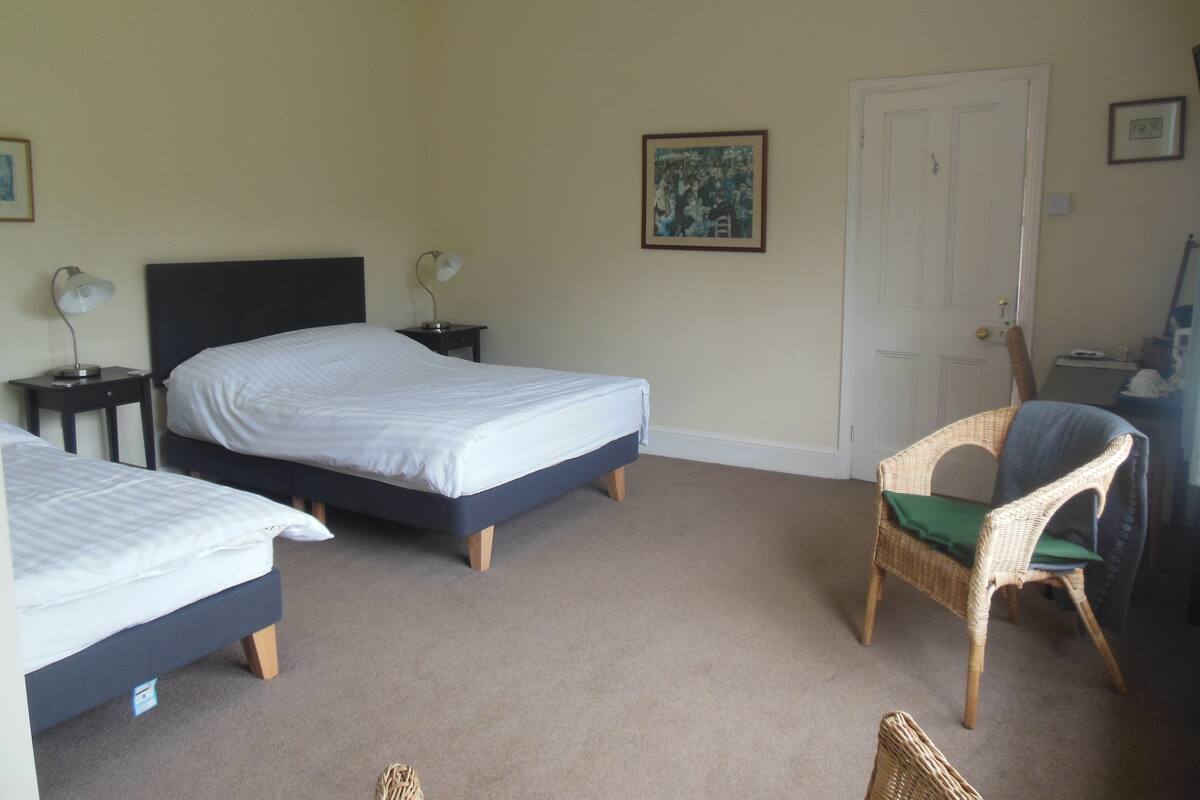A hotel room with two single beds, a chair, a desk, and a door.