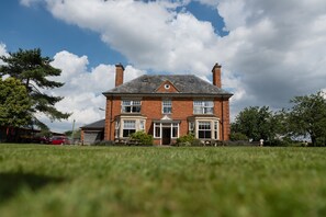 A large brick house with a central entrance, two chimneys, and a sloped roof.