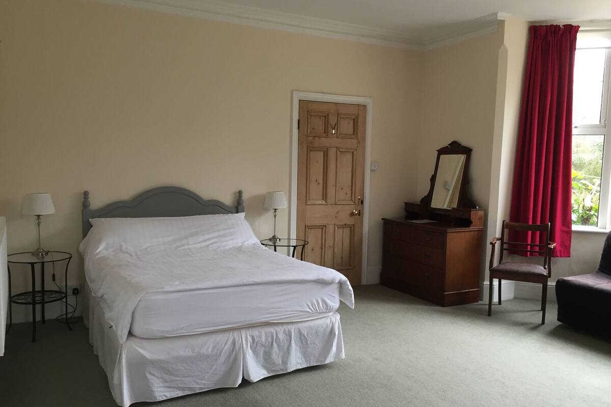 A neatly arranged bedroom with a bed, a dresser, a chair, and a window with curtains.