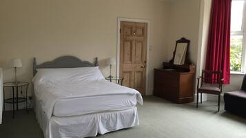 Un dormitorio ordenado con cama, cómoda, silla y ventana con cortinas.