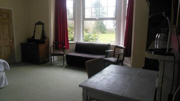 Een kamer met een bank, twee stoelen, een tafel, een piano en een raam met gordijnen.
