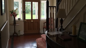 Un couloir avec un escalier en bois, une porte donnant sur l’extérieur et une table sur laquelle se trouvent une lampe et des livres.