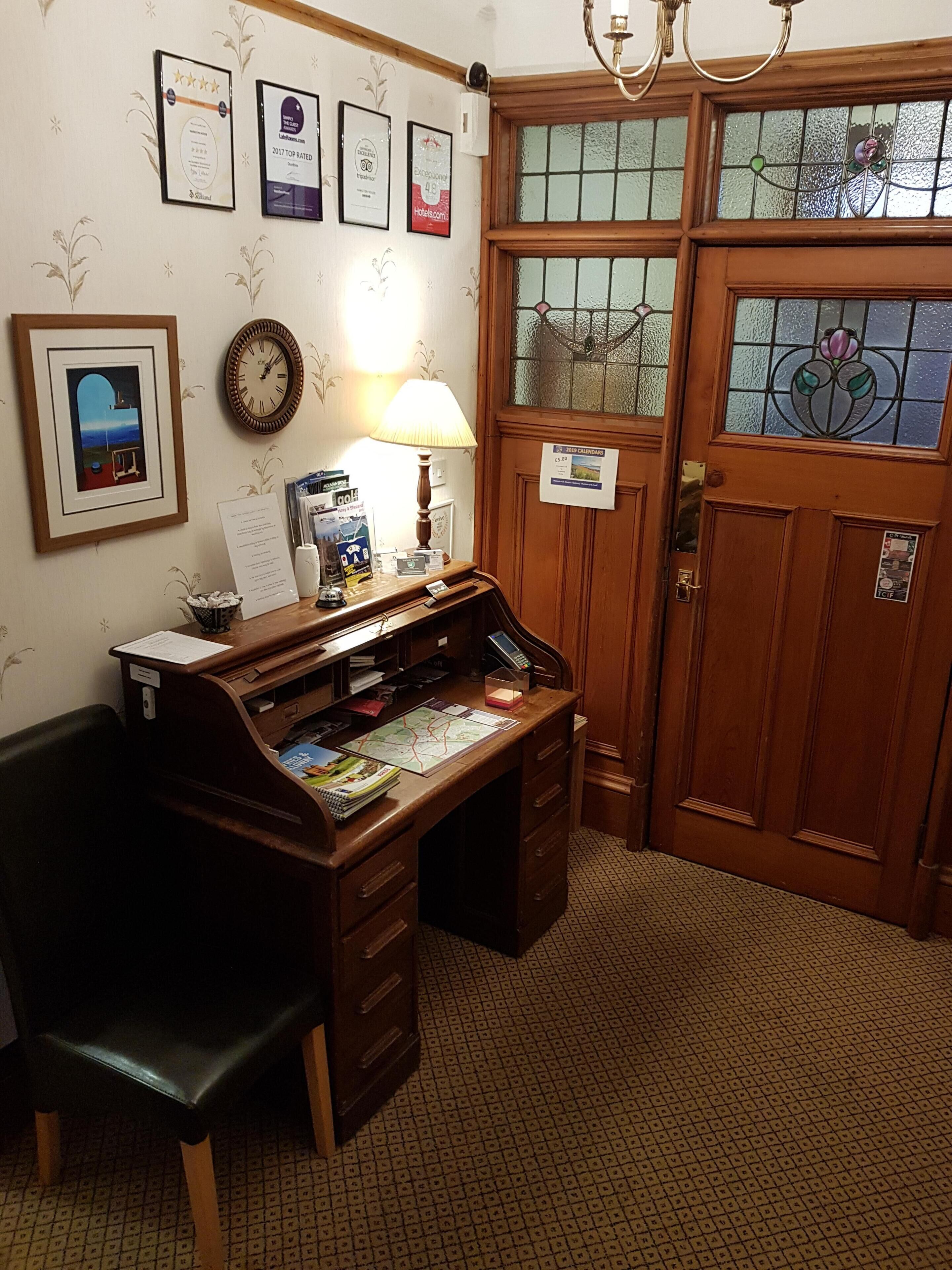 A reception desk with a lamp, framed certificates, and a clock.