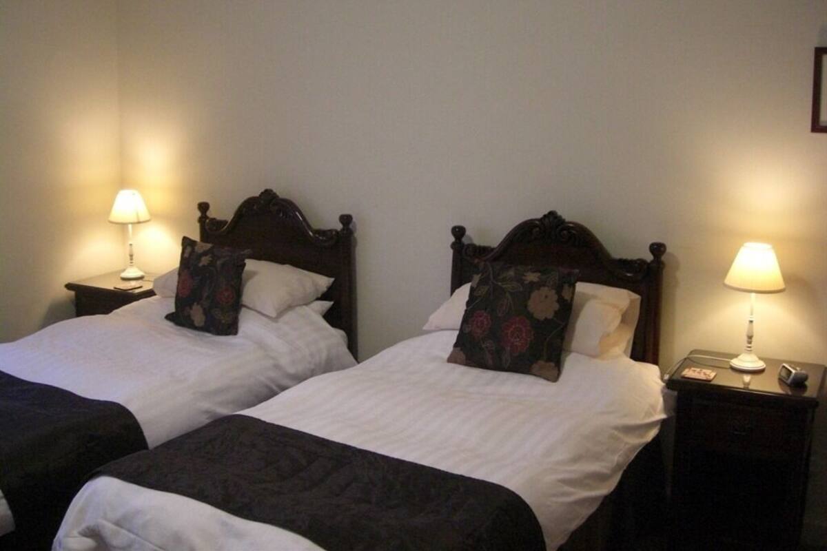 Two single beds with wooden headboards, white linens, and floral-patterned pillows. Each bed has a bedside table with a lamp and a small clock.
