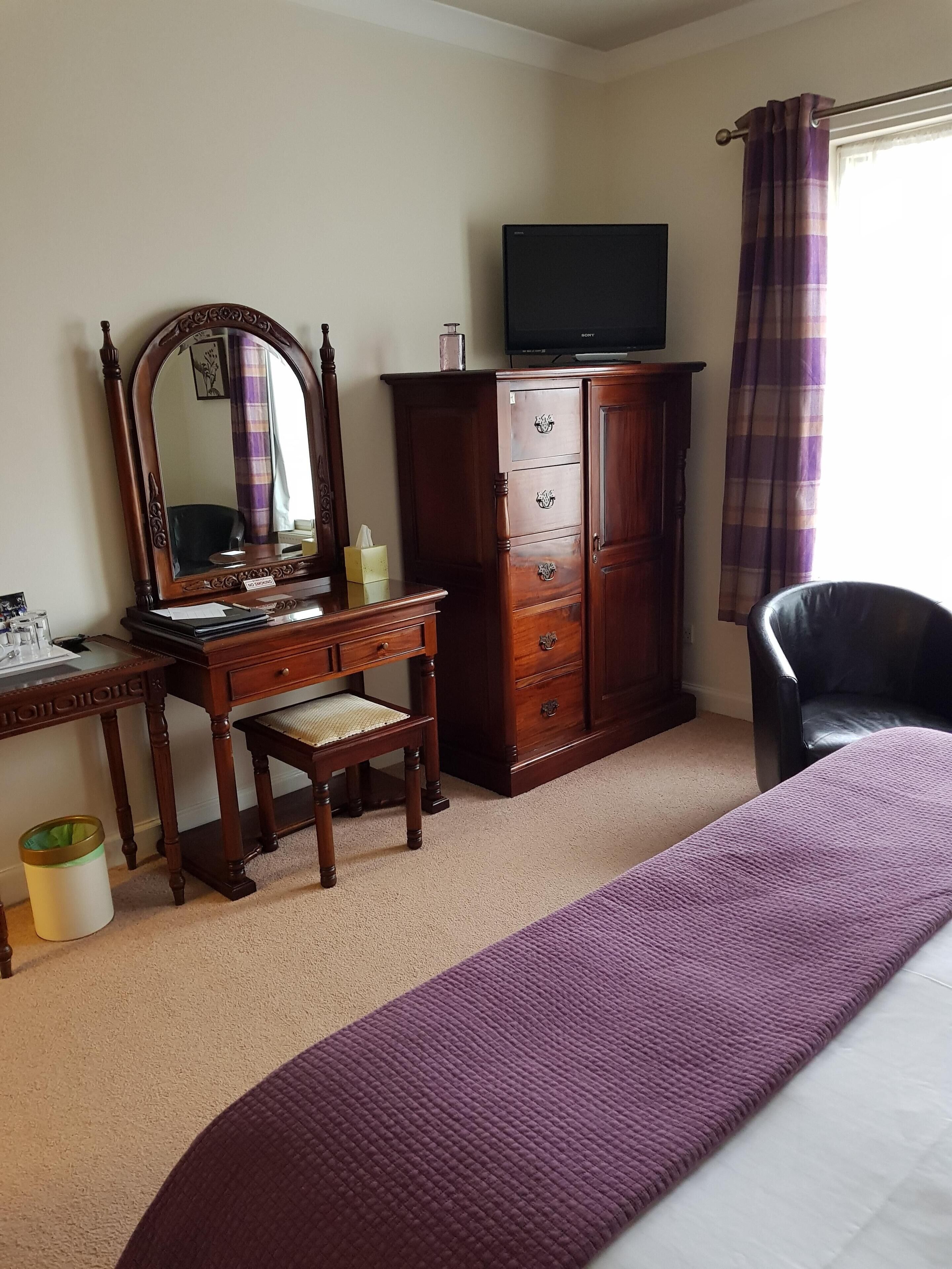 A bedroom with a wooden dresser, a mirror, a television, a chair, and a bed.