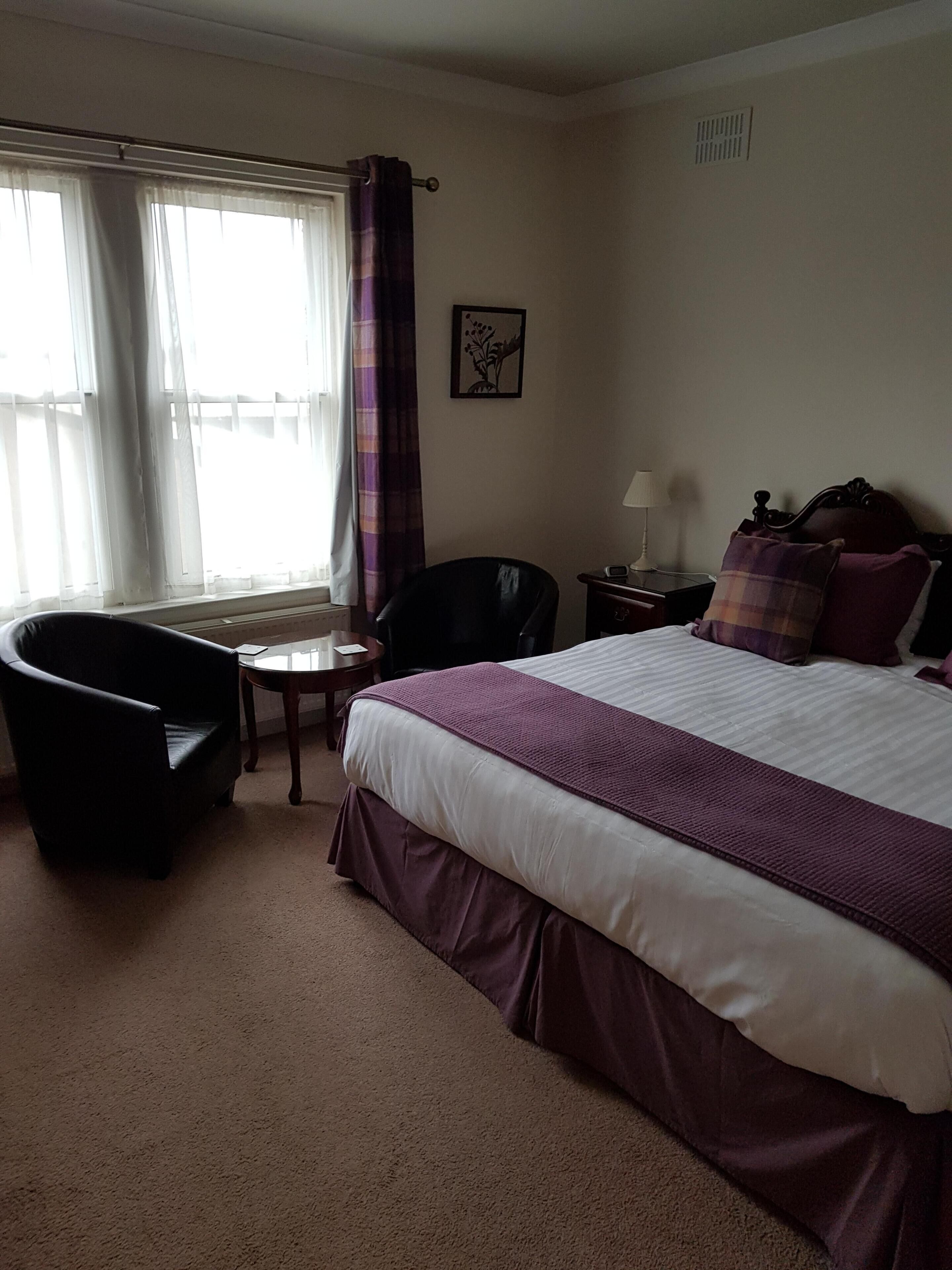 A hotel room with a bed, a chair, a small table, and a nightstand.
