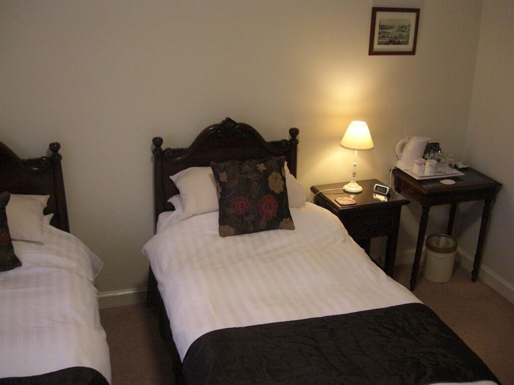 A hotel room with two single beds, a nightstand with a lamp, a telephone, and a trash can.