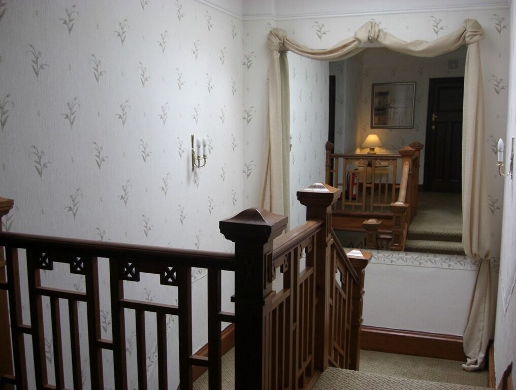 Una escalera con barandilla de madera, un espejo con marco decorativo y una lámpara sobre una mesa al fondo.
