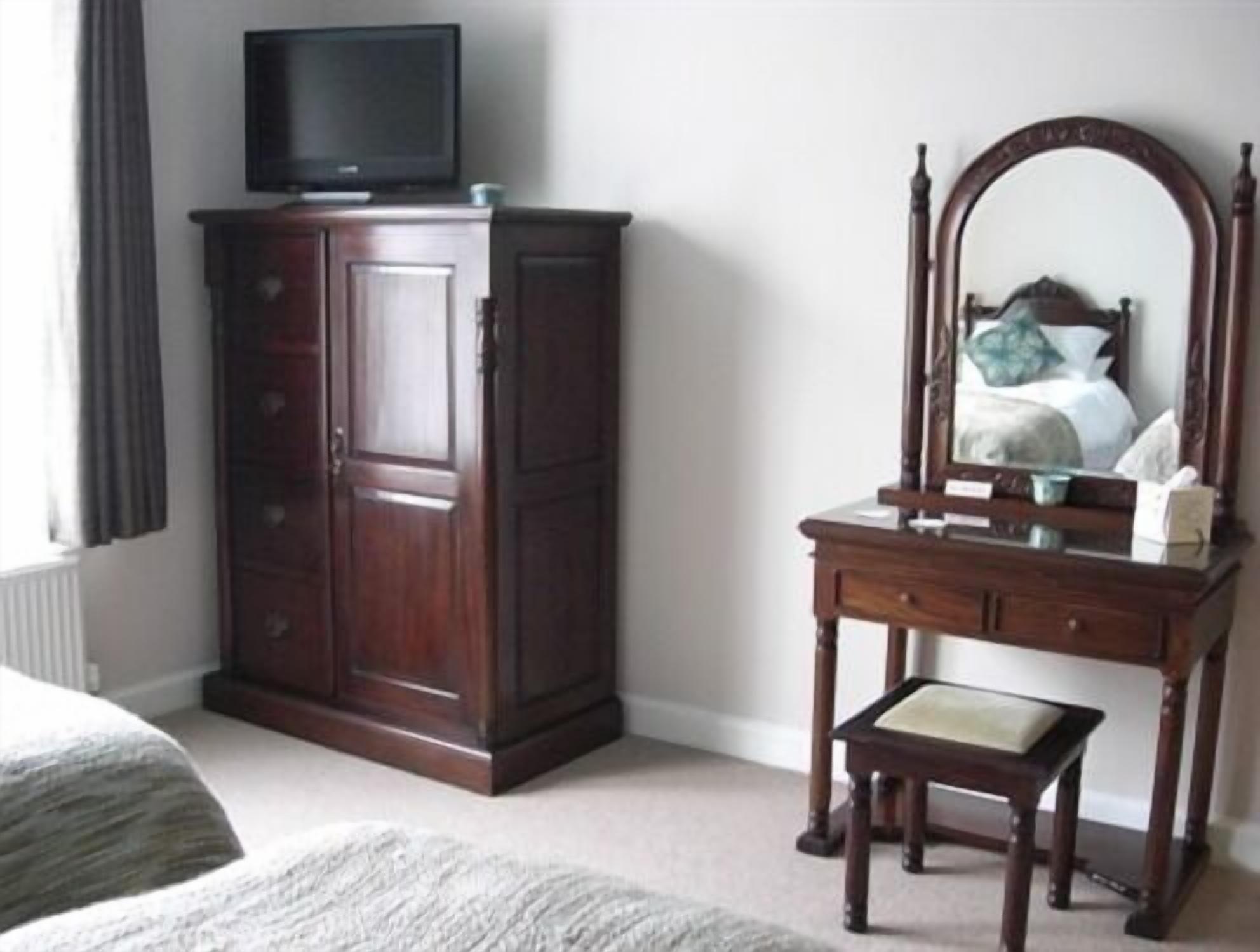 Un dormitorio con un armario de madera, una mesita de noche con espejo y un televisor encima del armario.