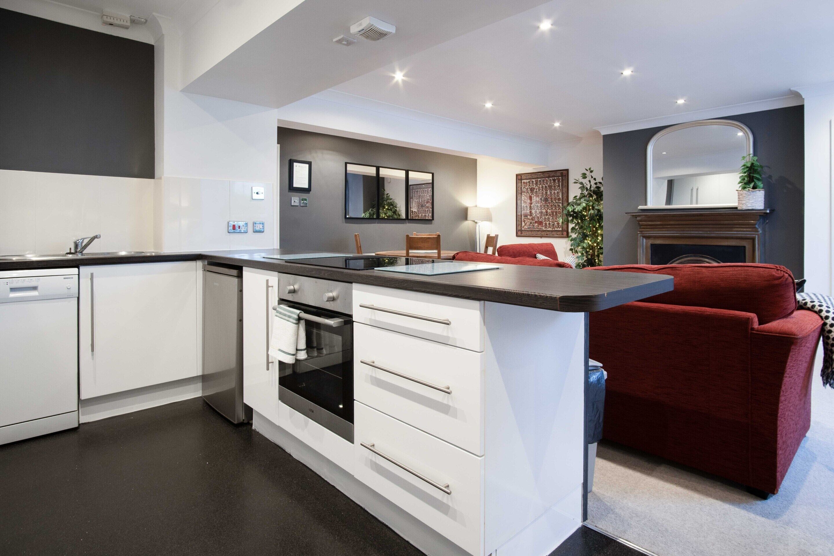 A modern kitchen with white cabinetry, a central island, and a red sofa in the living area.