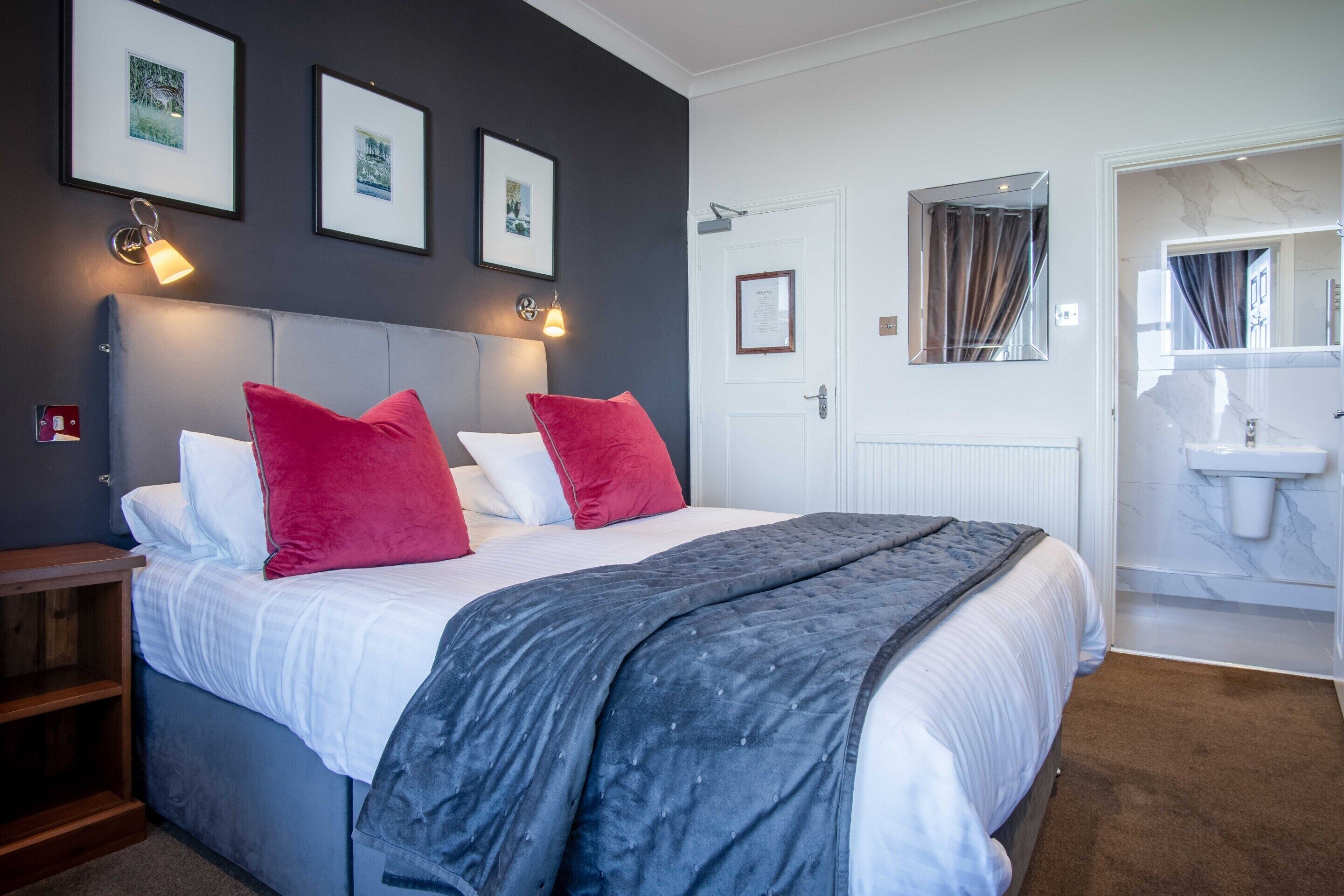 A bedroom with a bed, a nightstand, a bedside table, a wall-mounted light, and a framed picture.