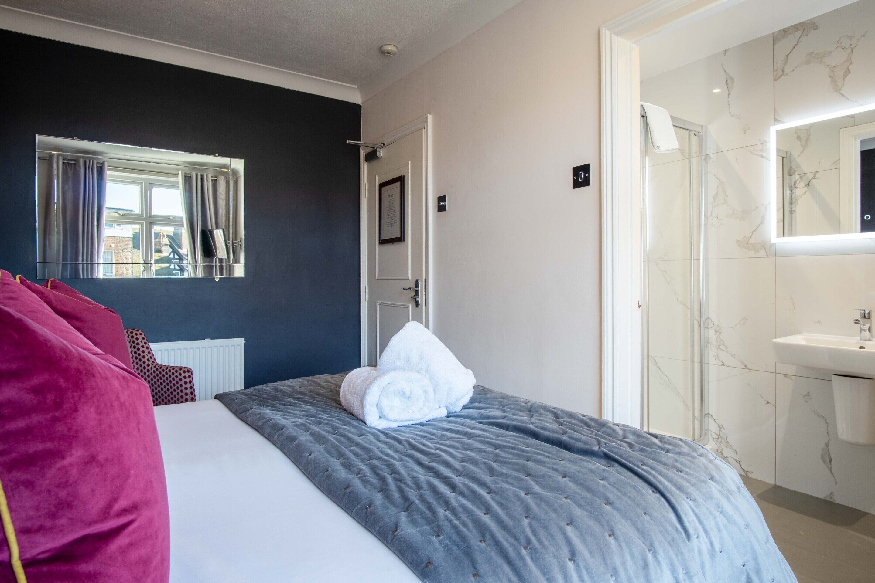 A hotel room with a bed, a window with curtains, a bathroom with a mirror and sink, and a door.