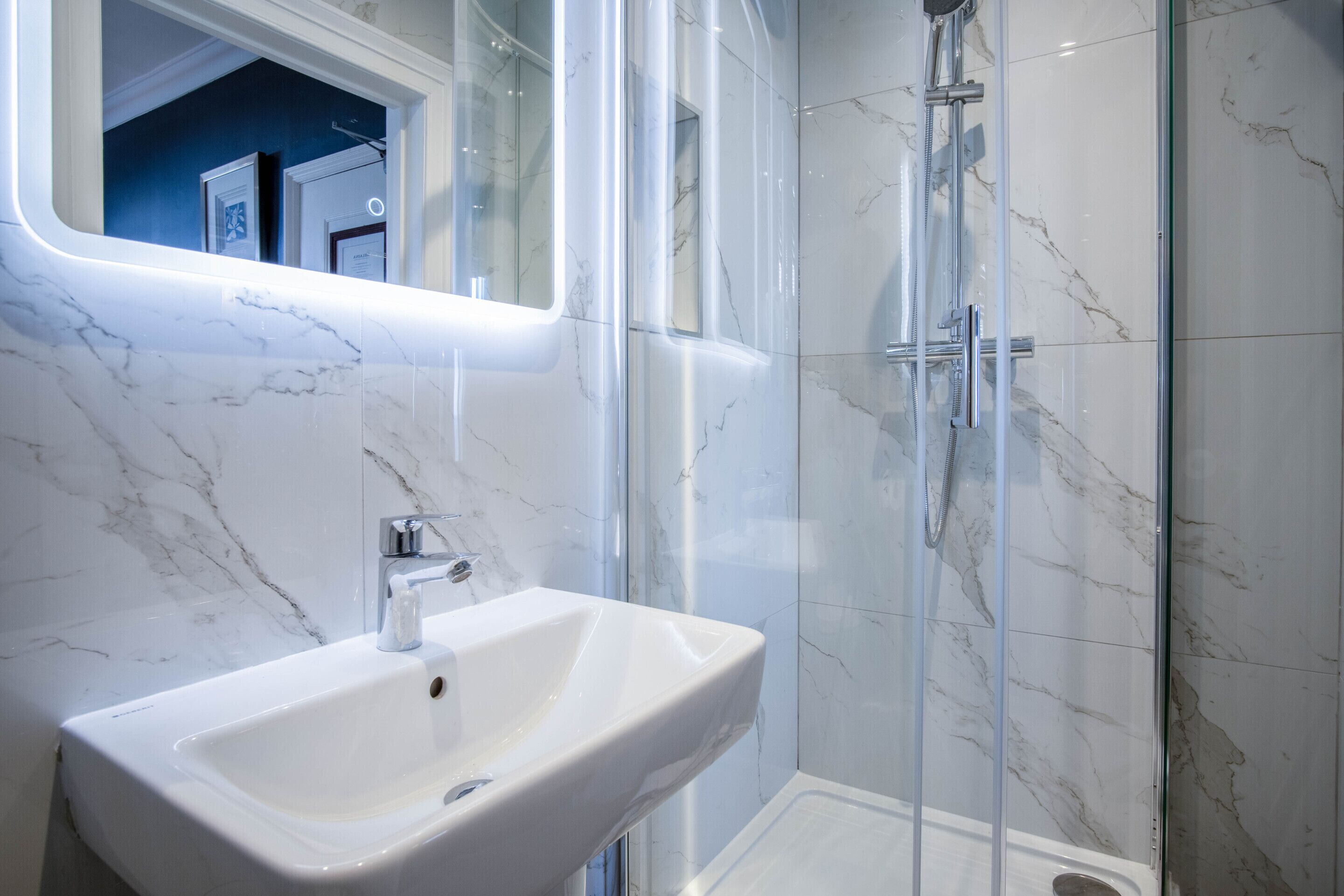 A modern bathroom with a white sink, a glass shower enclosure, and marble walls.