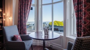 Ein gemütliches Zimmer mit einem runden Tisch, zwei Stühlen und Meerblick durch große Fenster.