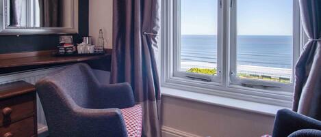 A room with a view of the sea, a desk with a mirror, and two chairs.