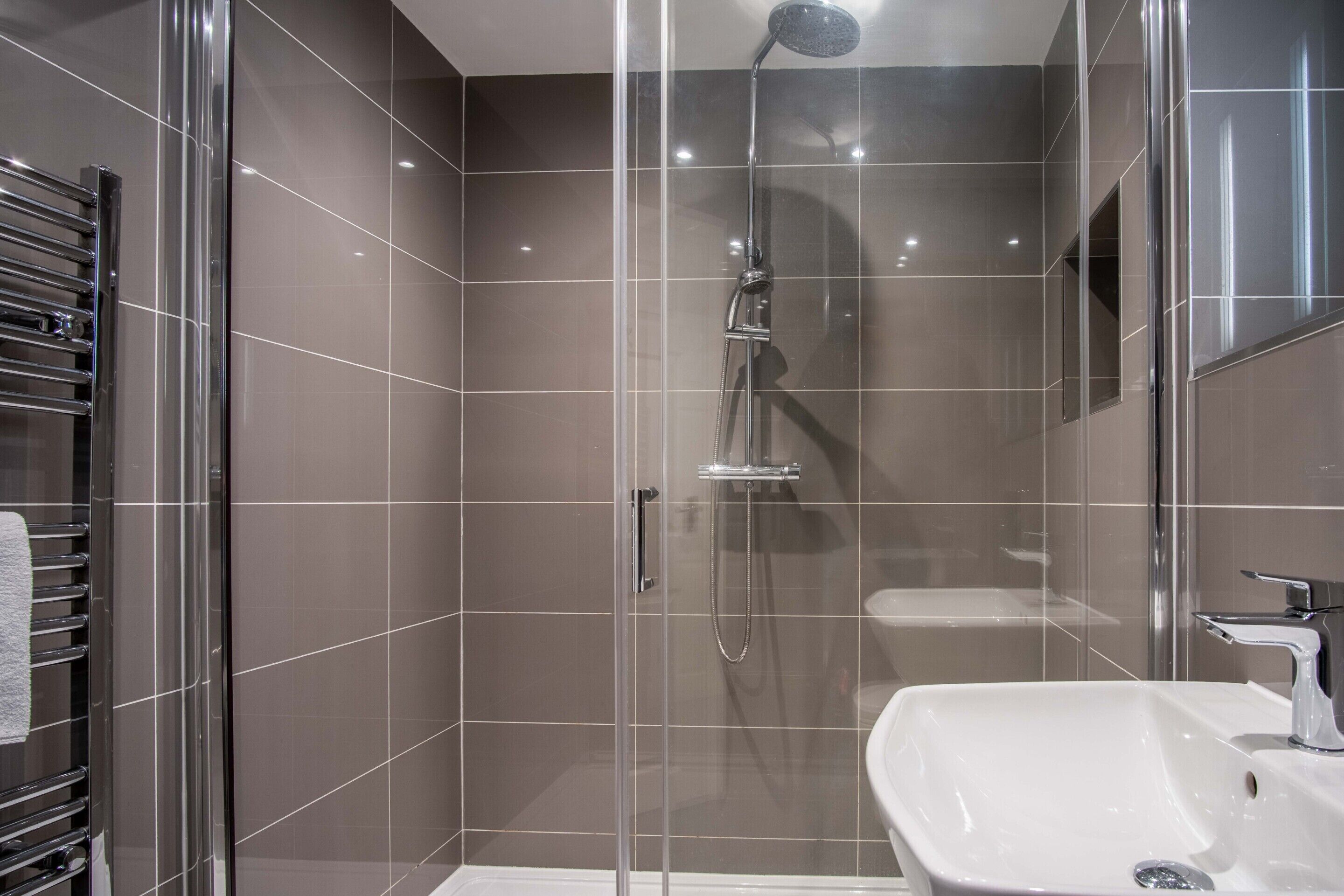 A modern bathroom with a glass-enclosed shower, a white sink, and a towel rack.