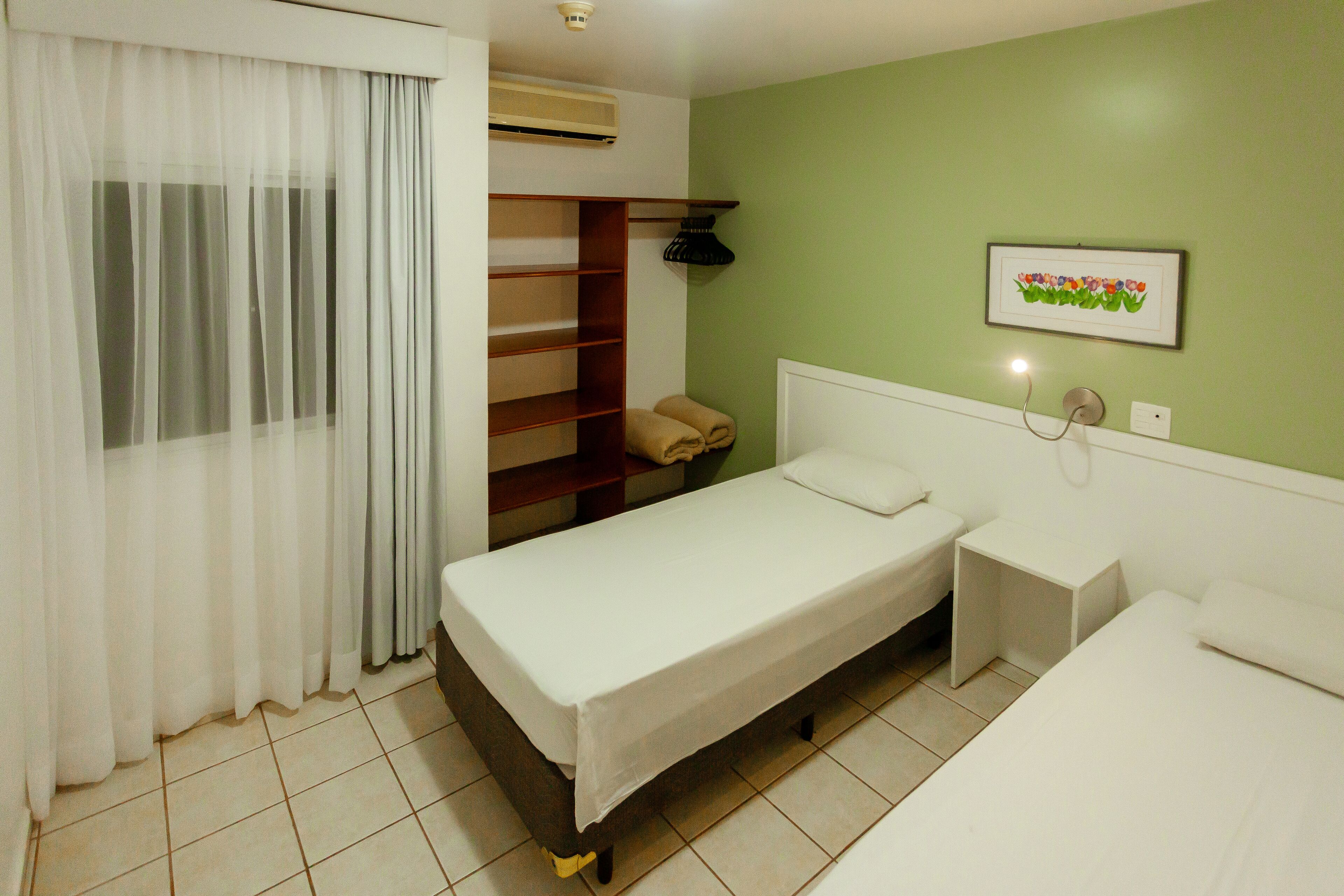 A hotel room with a bed, bedside table, and a shelf with towels.