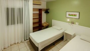 A hotel room with a bed, bedside table, and a shelf with towels.