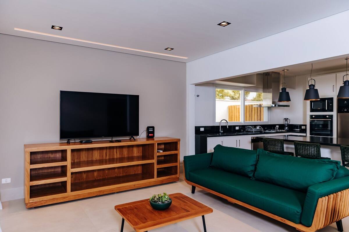 A modern living room with a flat-screen TV, wooden entertainment unit, green sofa, and a small coffee table.