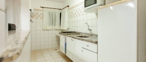 A kitchen with white cabinets, a granite countertop, a built-in microwave, and a stainless steel sink.