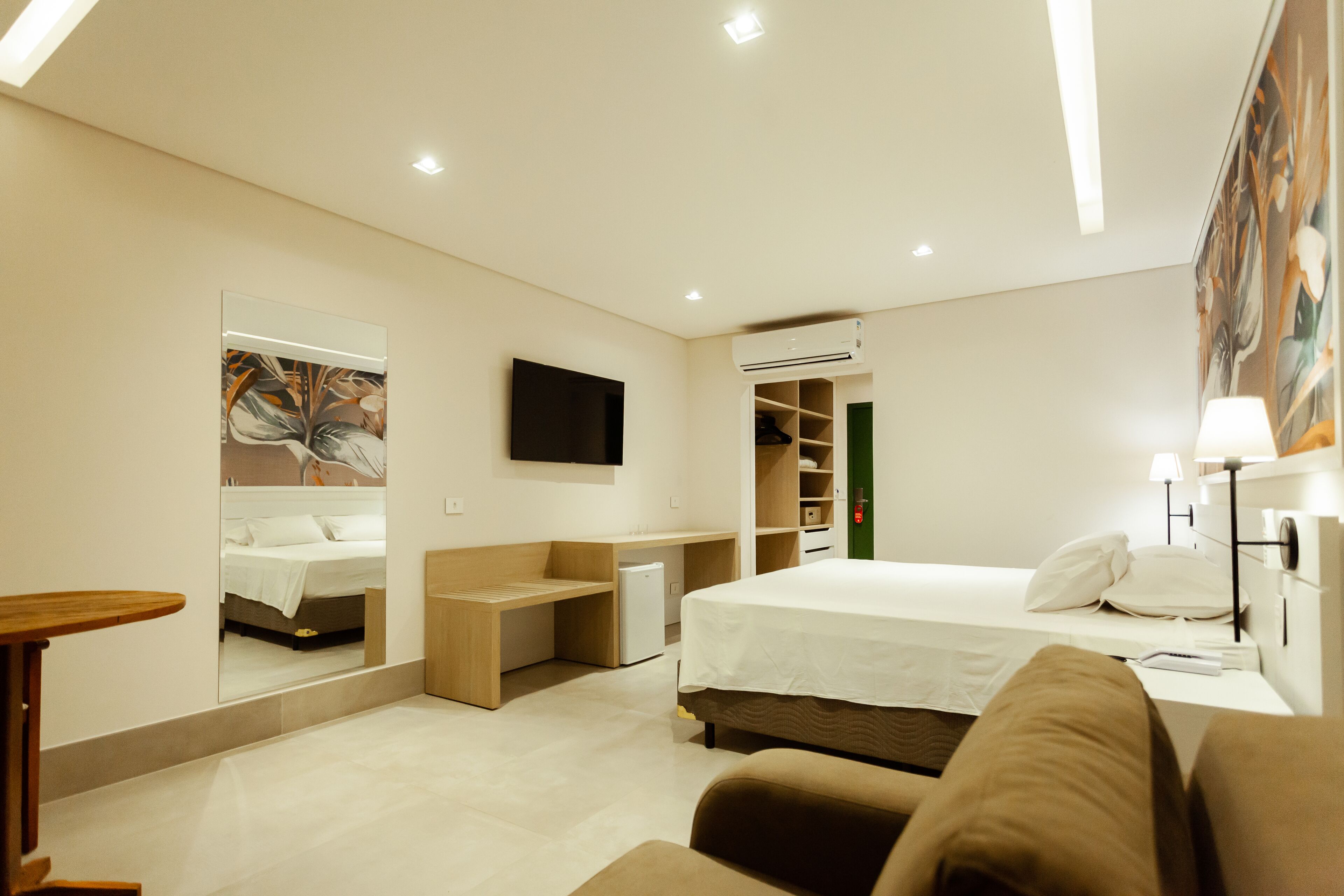 Una habitación de hotel moderna con una cama, un escritorio, una silla, una mesita, un televisor y un armario.