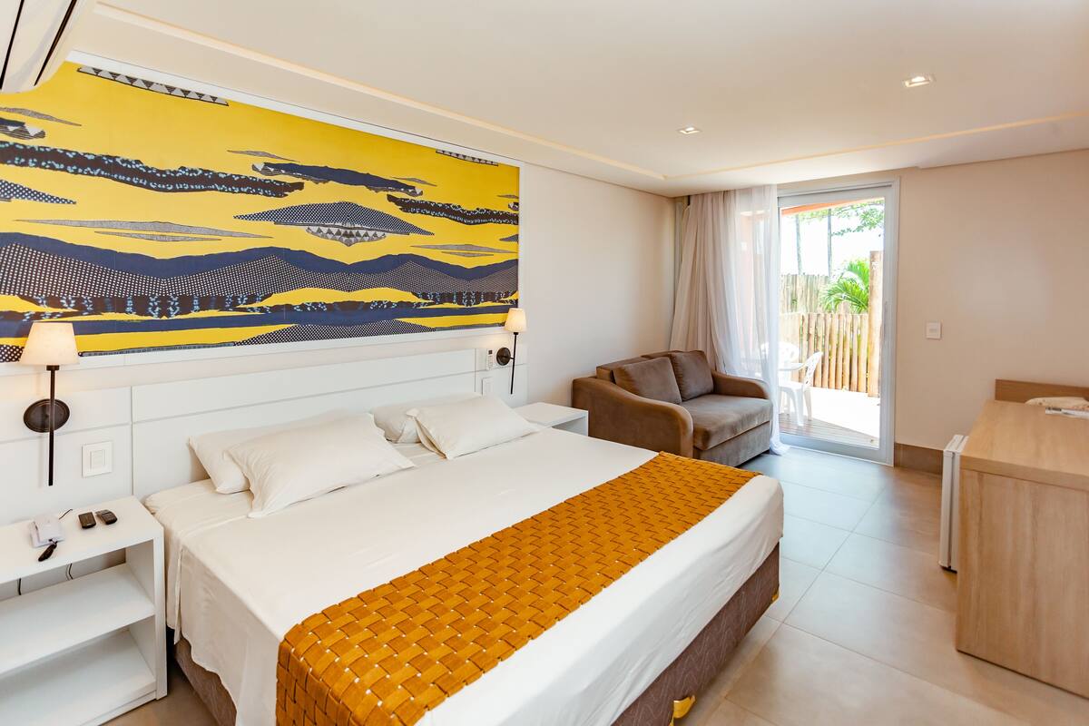 A hotel room with a large bed, a sofa, a desk, and a large window.